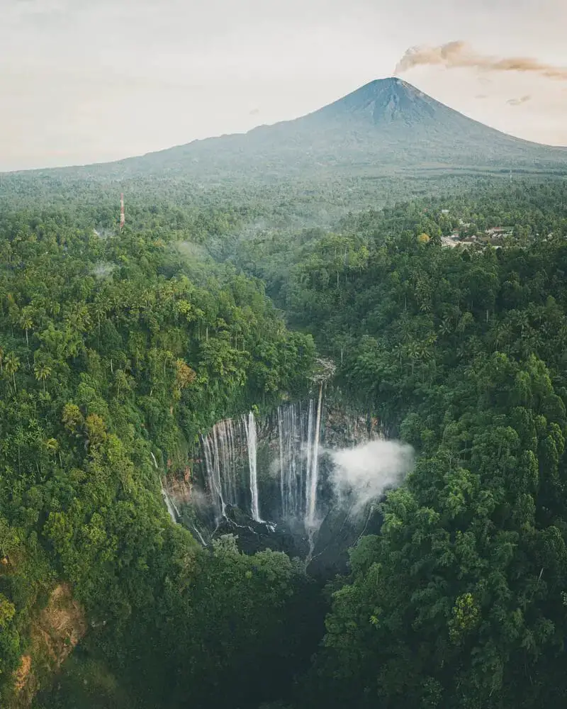 Aerial picture of Tumpak Sewu waterfall - a must visit when backpacking in Java and mount Semeru in the background.
