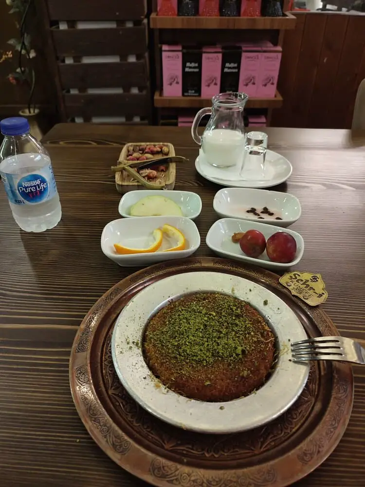 Kunefe with all side dishes - a slive of apple, watermelon, milk, green pistachios, plums and 2 orange slices.