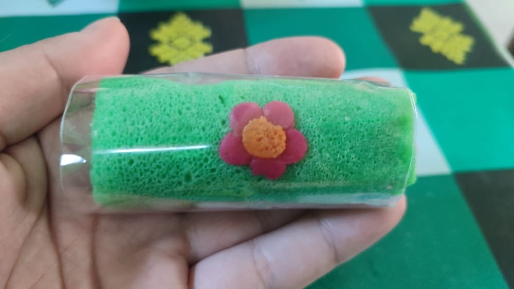 A single green dadar gulung wrapped in plastic, with a cute flower decoration