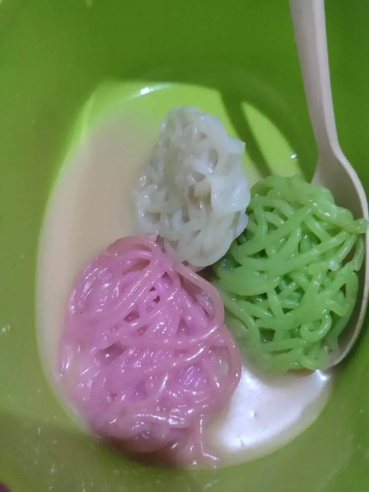Three different colored kue putu mayang pieces that look like knotted thread in a soup of coconut milk and sugar.