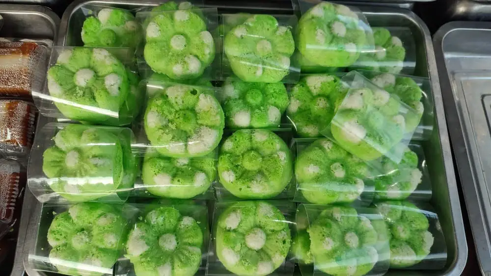 A tray of green, flower-shaped kue putu ayu, individually wrapped in plastic