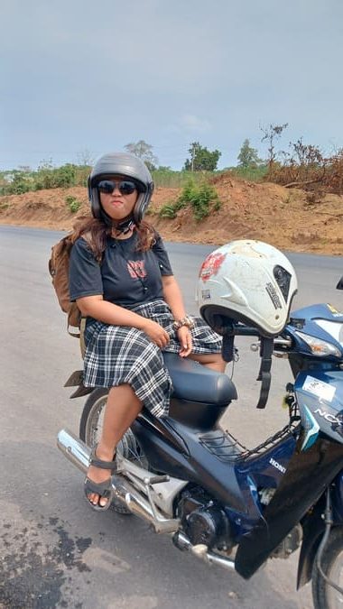 Yulli sitting on the pillion seat of a parked motorcycle