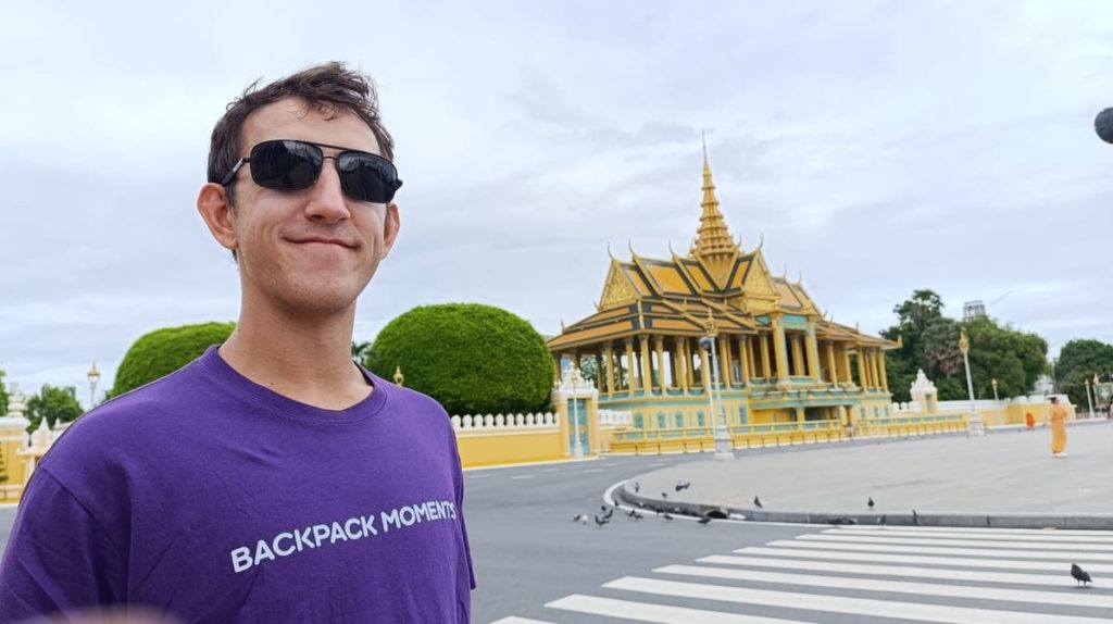 Simon posing in a purple "Backpack Moments" t-shirt in front of the Royal Palace in Phnom Penh
