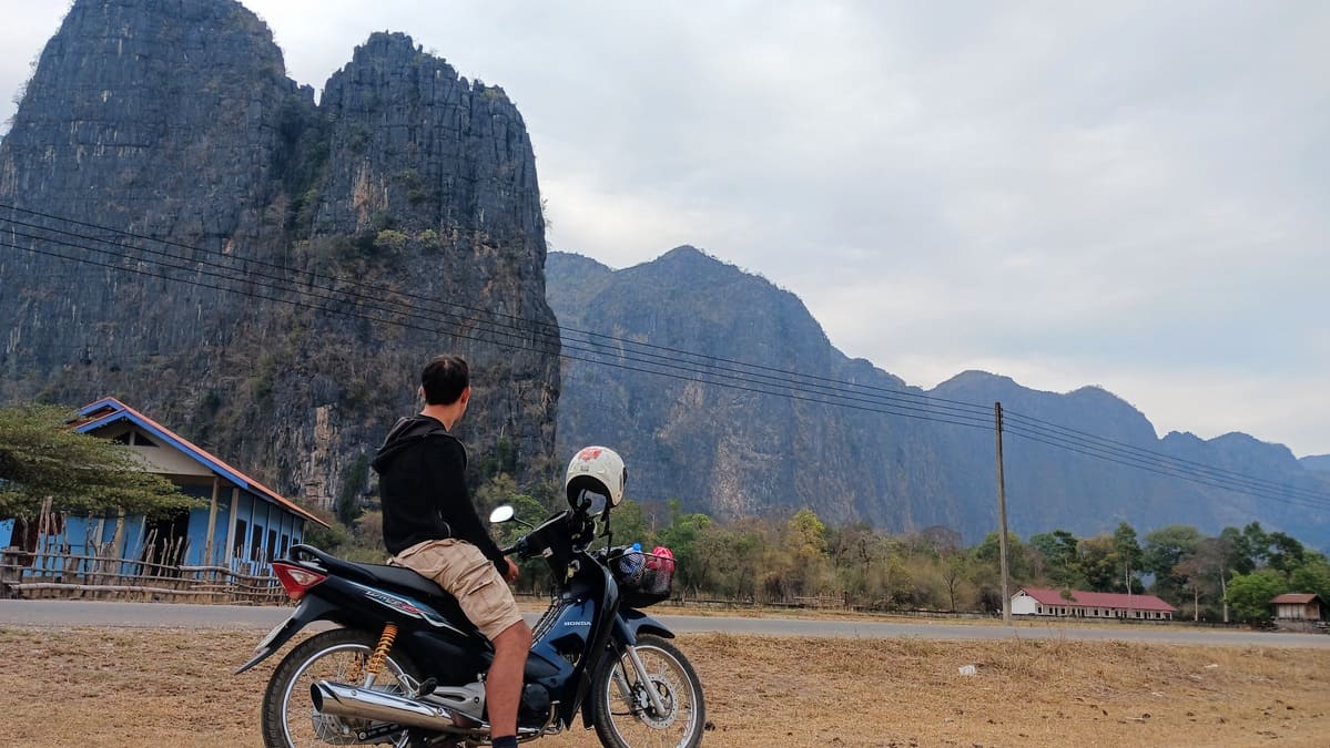 Simon sitting on a motorcycle looking at the mountains around Kong Lor