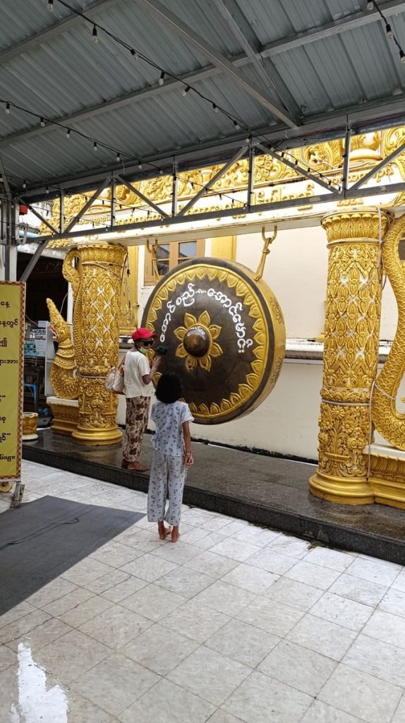 a woman and a girl in front of a giant gong in a Buddhist Pagoda