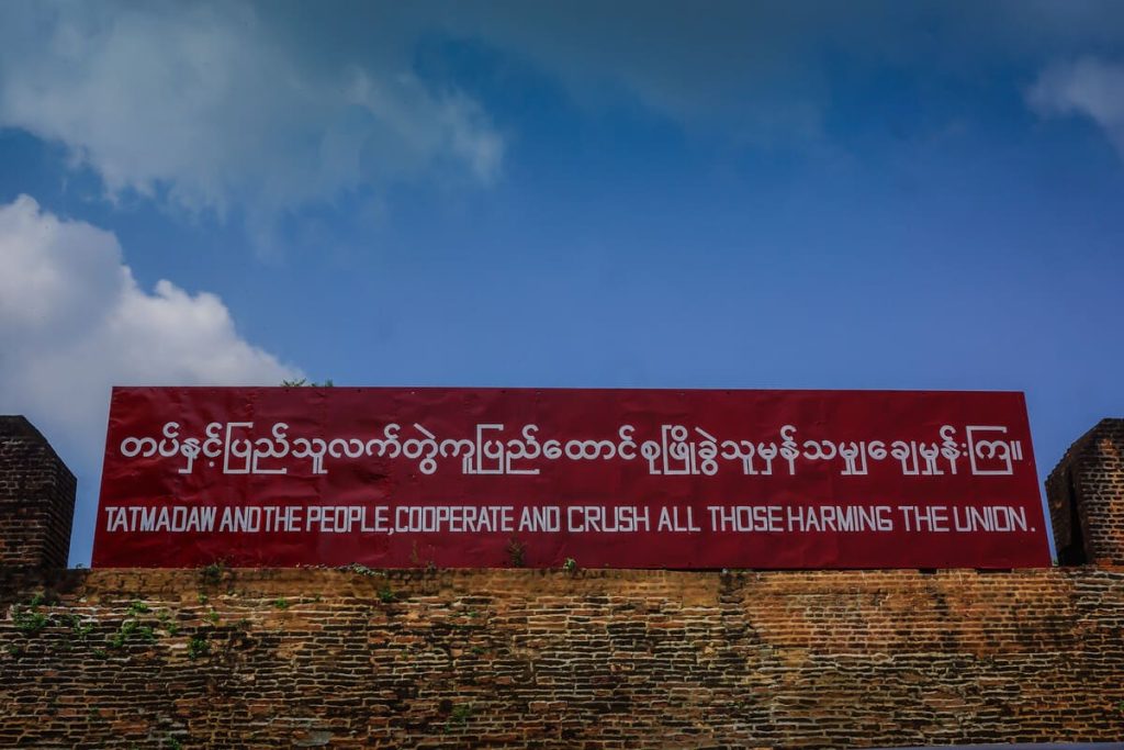 a Tatmadaw propaganda sign that reads "Tatmadaw and the people, cooperate and crush all those harming the union."