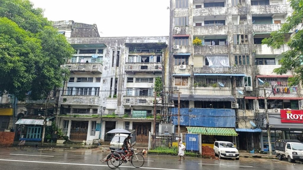 A man on a tricycle and a barefoot man walking on the streets of Yangon