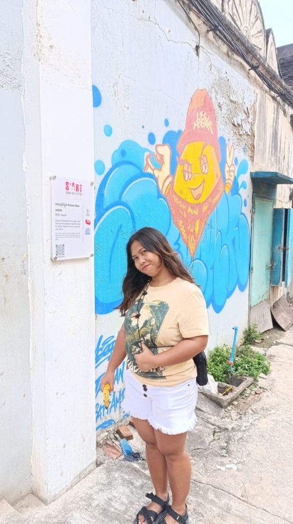 Yulli sitting next to a mural showing the Sun spraying clouds.