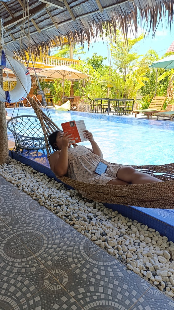 Yulli lying in a hammock, reading a book by the pool in a hostel