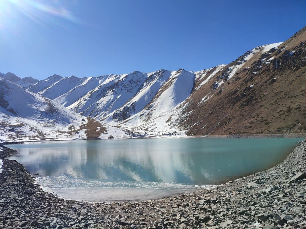 A lake in Kyrgyzstan with snow-capped mountains behind it.