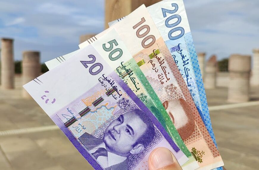 A hand holding Moroccan Dirham banknotes in front of the Koutobia Mosque in Marrakech