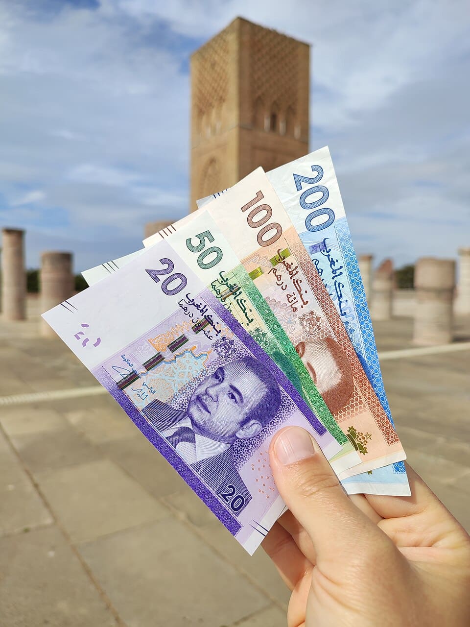 A hand holding Moroccan Dirham banknotes in front of the Koutobia Mosque in Marrakech