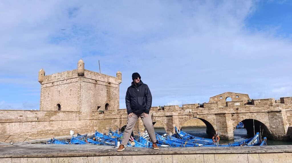 Simon on top of the wall surrounding the blue boats in Essaouira